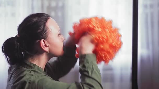 Una mujer delante de un espejo se pone una peluca de payaso con rizos rojos. — Vídeo de stock
