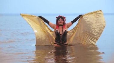 Siyah korseli bir şeytan şeklinde altın kanatlı bir kadın gölde kanat çırpan bir suda zarifçe yürür..