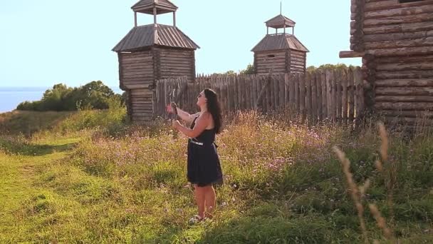 Женщина-блогер ведет блог со своего телефона и рассказывает о деревянной крепости на вершине горы. — стоковое видео