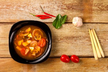Geleneksel Tayland çorbası Tom Yam ahşap bir masada, sarımsak ve limon otunun yanında, kaffir limonu, kırmızı biber ve kiraz..