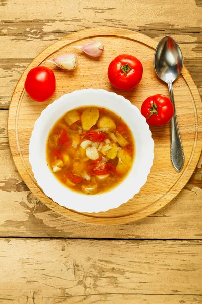 나무로 만든 둥근 받침대 위에 흰 접시를 놓고 토마토와 마늘 옆에 숟가락을 놓은 포시니 버섯 수프. — 스톡 사진