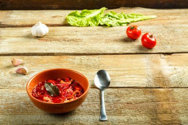 Sebzelerin yanındaki ahşap masada tavuklu kil borş tabağı..