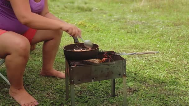 Une femme mélange des saucisses râpées avec des champignons dans une poêle sur les charbons. — Video