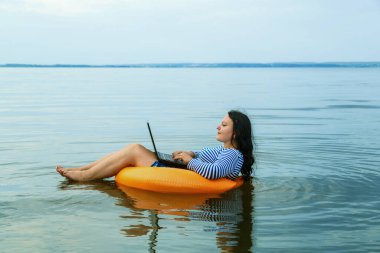 Tatildeki kadın, sabahları yüzme çemberinde dizüstü bilgisayarla uzaktan çalışıyor..
