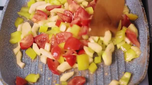 A abobrinha cortada com pimenta e tomate em uma frigideira é mexida por uma espátula de madeira. — Vídeo de Stock