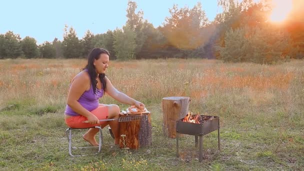 A brunette woman by the fire in the evening lays chicken on the grill for barbecue. — Stock Video