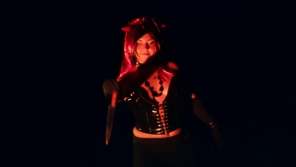 Una donna a forma di diavolo con le corna di notte vicino al fuoco con un coltello balla una danza rituale nel fumo. — Video Stock