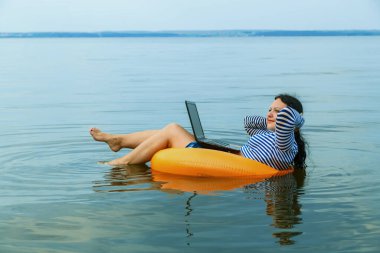 Kadın sabah sularında yüzme çemberinde dizüstü bilgisayarla uzaktan çalışıyor..