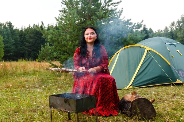 Młoda Cyganka grilluje mięso w pobliżu namiotu. — Zdjęcie stockowe
