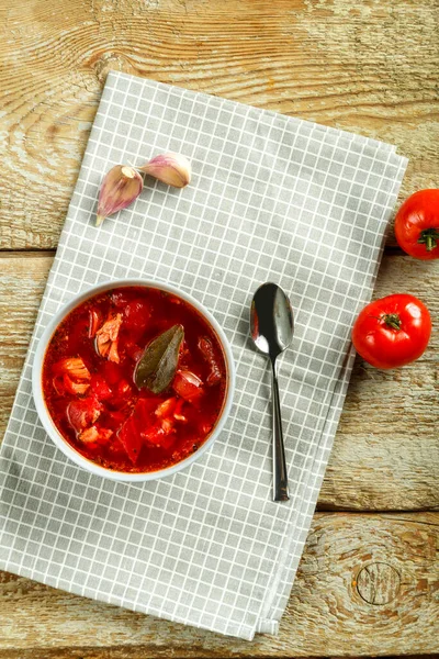 Un piatto di borscht con pollo su un tovagliolo con un cucchiaio su un tavolo di legno accanto all'aglio e ai pomodori. — Foto Stock