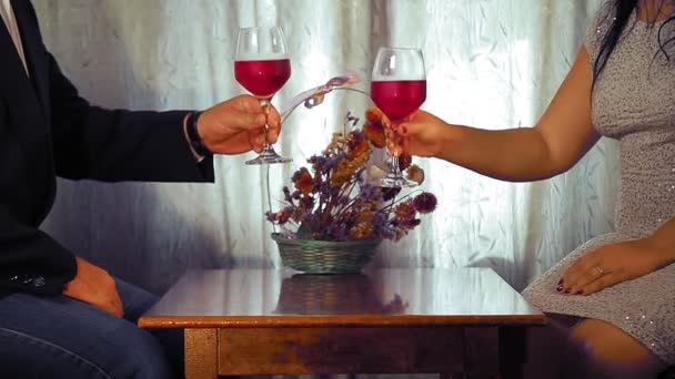 Un hombre y una mujer sin rostro celebran la cita en la mesa y beben vino tinto — Vídeos de Stock