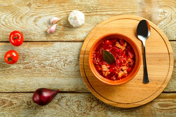 Um prato de borscht de barro com frango com uma colher em uma mesa de madeira em um suporte redondo. — Fotografia de Stock