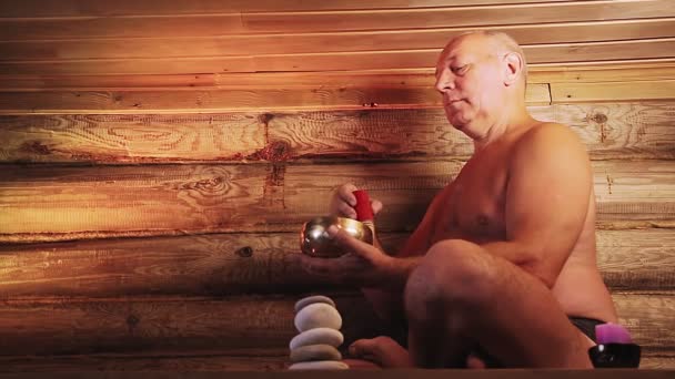 Um homem em um salão de spa com velas medita com uma tigela cantando — Vídeo de Stock