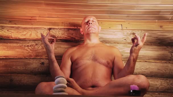 Staruszek w saunie ze świecami medytuje. — Wideo stockowe