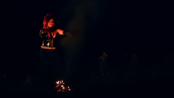 Uma mulher na forma de um diabo com chifres à noite junto ao fogo com uma faca dança uma dança ritual — Vídeo de Stock