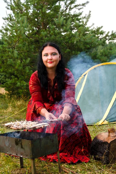 一个年轻的吉普赛妇女在靠近帐篷的烤架上烤肉，冒着浓烟。. — 图库照片