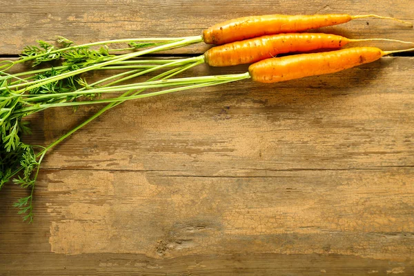 Tahta masa üzerindeki yeşil tepeli taze havuçları kopyala