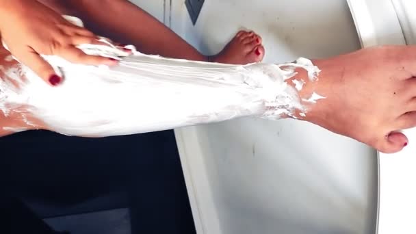 Egy nő a zuhany alatt borotválja a lábát és borotválja a lábát. Függőleges — Stock videók