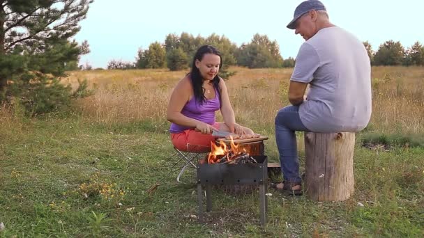 Un uomo e una donna in natura preparano carne per grigliare vicino al fuoco — Video Stock
