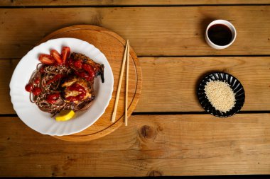 Soba tavuklu ve sebzeli soya soslu soba ve çubukların yanında susam tohumlu beyaz bir tabakta..