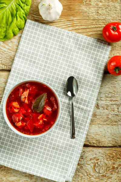 Un piatto di borscht con pollo su un tovagliolo con un cucchiaio su un tavolo di legno accanto all'aglio e ai pomodori. — Foto Stock