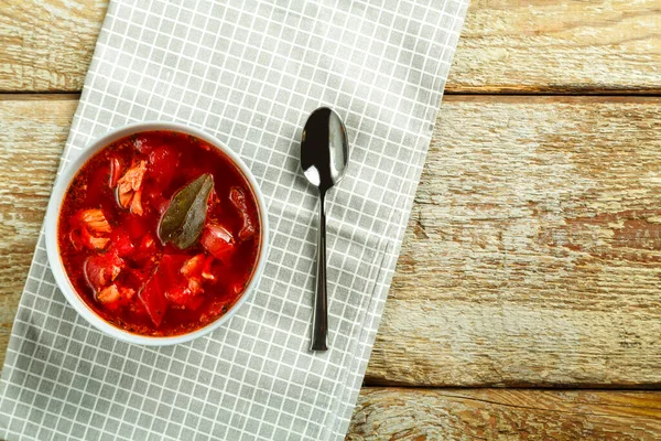 Un plato de borscht con pollo en una servilleta con una cuchara en una mesa de madera. —  Fotos de Stock