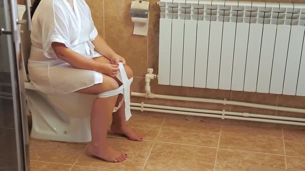 Egy fehér köpenyes nő ül a WC-n a mosdóban. Arc nélküli lövés — Stock videók