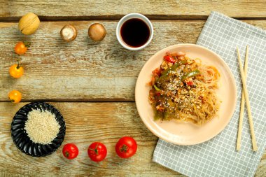 Çubukların, soya sosunun, sebzelerin ve susam tohumlarının yanındaki peçetenin üzerinde sebze ve mantarlı bir tabakta..