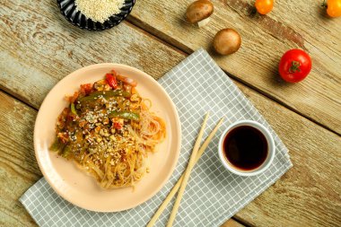 Çubuk ve soya sosu domatesleri ve susam tohumlarının yanındaki peçetenin üzerinde sebze ve mantarlı Funchoza..