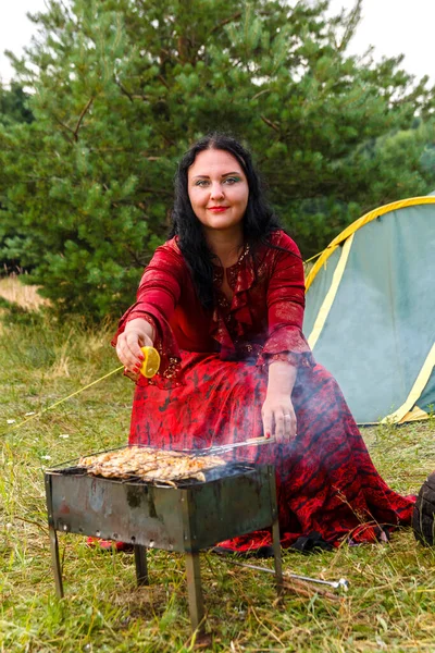 一个年轻的吉普赛妇女在靠近帐篷的烤架上烤肉，冒着浓烟。. — 图库照片