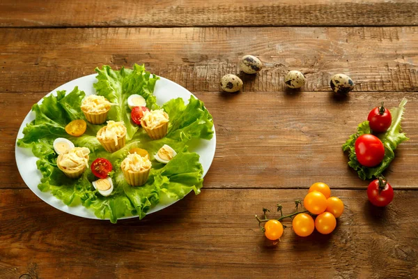 Tartaletas con queso y ajo en un plato con ensalada de cereza y huevos de codorniz en una mesa de madera. — Foto de Stock