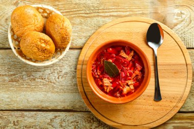 Bir tabak kil borş, tavuklu, ahşap bir masada kaşık kepekli çöreğin yanında..