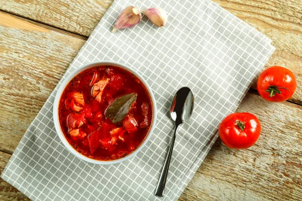 一盘罗宋汤，餐巾上有鸡肉，餐桌上有勺子，旁边有大蒜和西红柿. — 图库照片