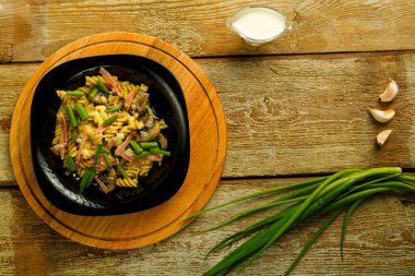 Jambonlu ve mantarlı siyah tabak ve kremalı sos. Masanın üzerinde çatal ve malzemelerin yanında..