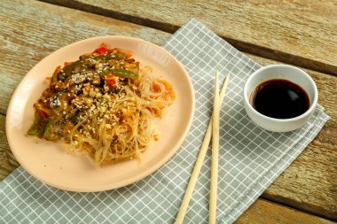 Çubuk ve soya sosunun yanındaki peçetenin üzerinde sebze ve mantarlı Funchoza..