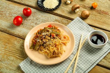 Çubukların, soya sosunun, sebzelerin ve susam tohumlarının yanındaki peçetenin üzerinde sebze ve mantarlı bir tabakta..