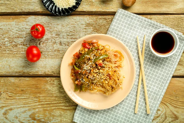 Funchoza con verduras y champiñones en un plato en una servilleta cerca de palitos y salsa de soja tomates y semillas de sésamo. —  Fotos de Stock