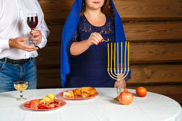 Żydowska rodzina bez twarzy, kobieta zapala świece w przeddzień Rosz Haszana w świeczniku. Mężczyzna trzyma szklankę dla Kiddusha.. — Zdjęcie stockowe