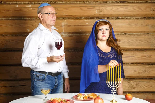 축제가 열리는 식탁에 앉아 있는 유대인 가족의 남편과 아내, 한 남자가 키디 쉬 여성을 위해 촛불을 들고 와인을 들고 있다.. — 스톡 사진