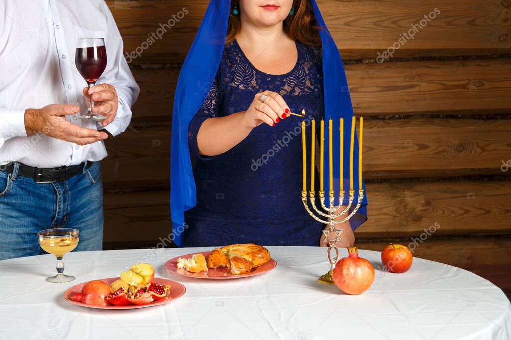 Jewish family without a face, a woman lights candles on the eve of Rosh Hashanah in a candlestick a man holds a glass for Kiddush.