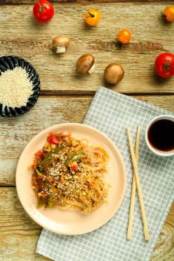 Çubukların, soya sosunun, sebzelerin ve susam tohumlarının yanındaki peçetenin üzerinde sebze ve mantarlı bir tabakta..