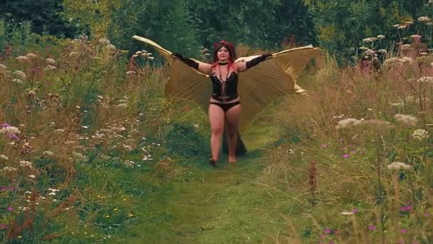 Жінка у вигляді демона в чорному корсеті з золотими крилами вибігає з лісу вздовж шляху. Часові кола — стокове відео