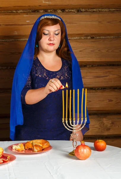 Een Joodse vrouw in een blauwe hoofdbedekking zal de kaarsen aansteken op de avond van Rosh Hashanah in een menorah-vormige kandelaar.. — Stockfoto