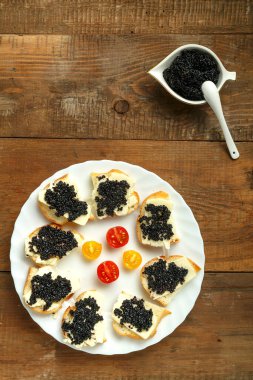 Siyah havyarlı sandviçler, beyaz bir tabakta, tahta bir masada, havyar tabağının yanında kaşık ile..