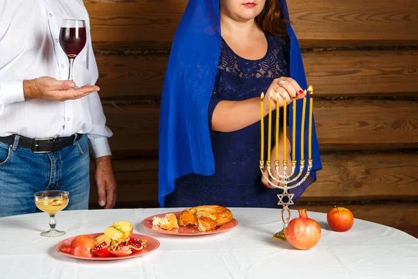 Família judia sem rosto, uma mulher acende velas na véspera de Rosh Hashanah em um castiçal um homem segura um copo para Kiddush. — Fotografia de Stock