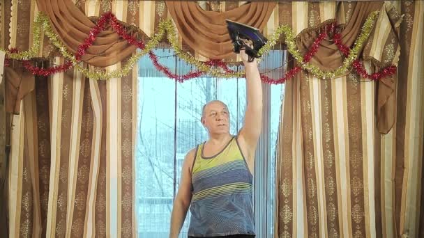 Een man in opleiding thuis met schudt spieren met een strijkijzer in plaats van een halter. — Stockvideo