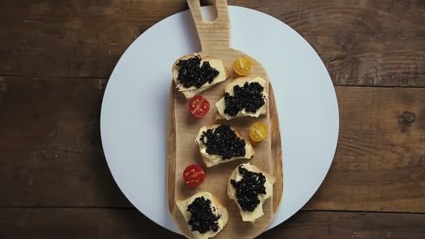 Los bocadillos con el caviar negro sobre la tabla de madera rotan en el círculo. — Vídeo de stock