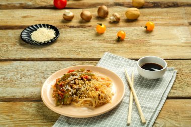 Çubukların, soya sosunun, sebzelerin ve susam tohumlarının yanındaki peçetenin üzerinde sebze ve mantarlı bir tabakta..