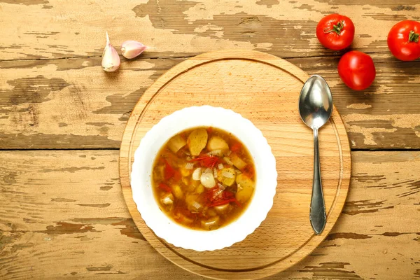 Zuppa di funghi porcini in un piatto bianco su un supporto rotondo in legno con un cucchiaio vicino ai pomodori. orizzontale — Foto Stock