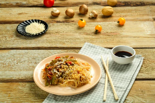 Çubukların, soya sosunun, sebzelerin ve susam tohumlarının yanındaki peçetenin üzerinde sebze ve mantarlı bir tabakta..